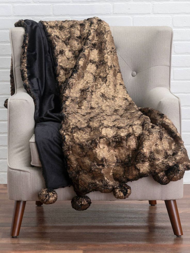 a chair with a blanket on it in front of a white brick wall and wooden floor