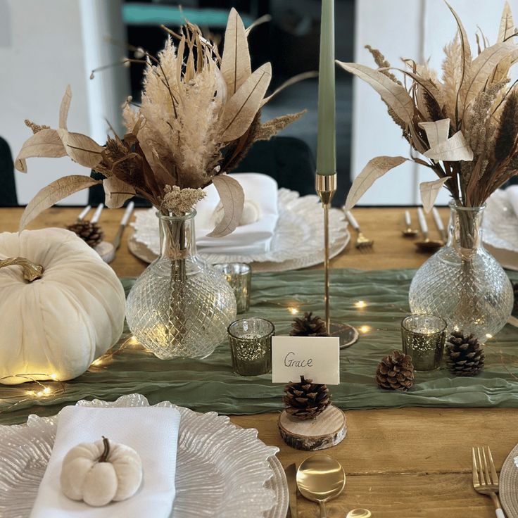 the table is set with white pumpkins, silverware and pamylum centerpieces