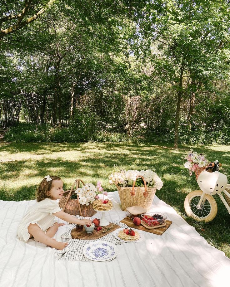 a woman sitting on top of a blanket next to a picnic table filled with food