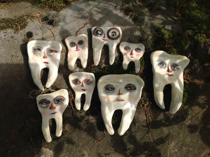 seven white teeth with eyes and nose painted to look like they have been placed on the ground