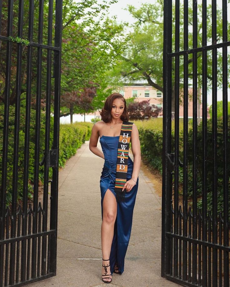 a woman in a blue dress is walking through an iron gate and posing for the camera