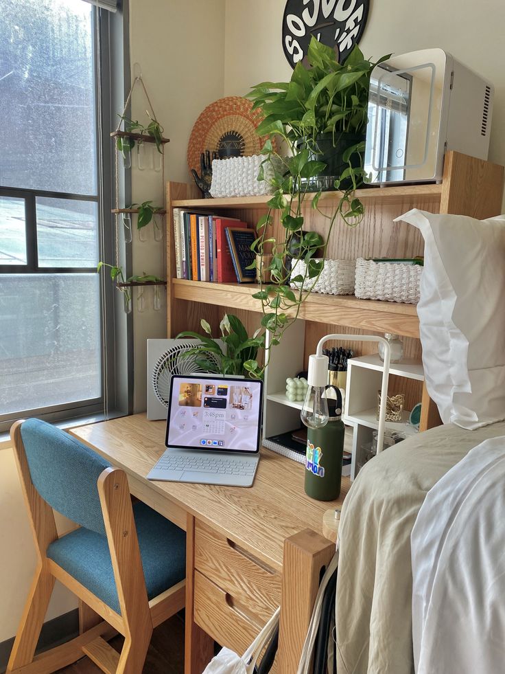 a laptop computer sitting on top of a wooden desk next to a bed and window