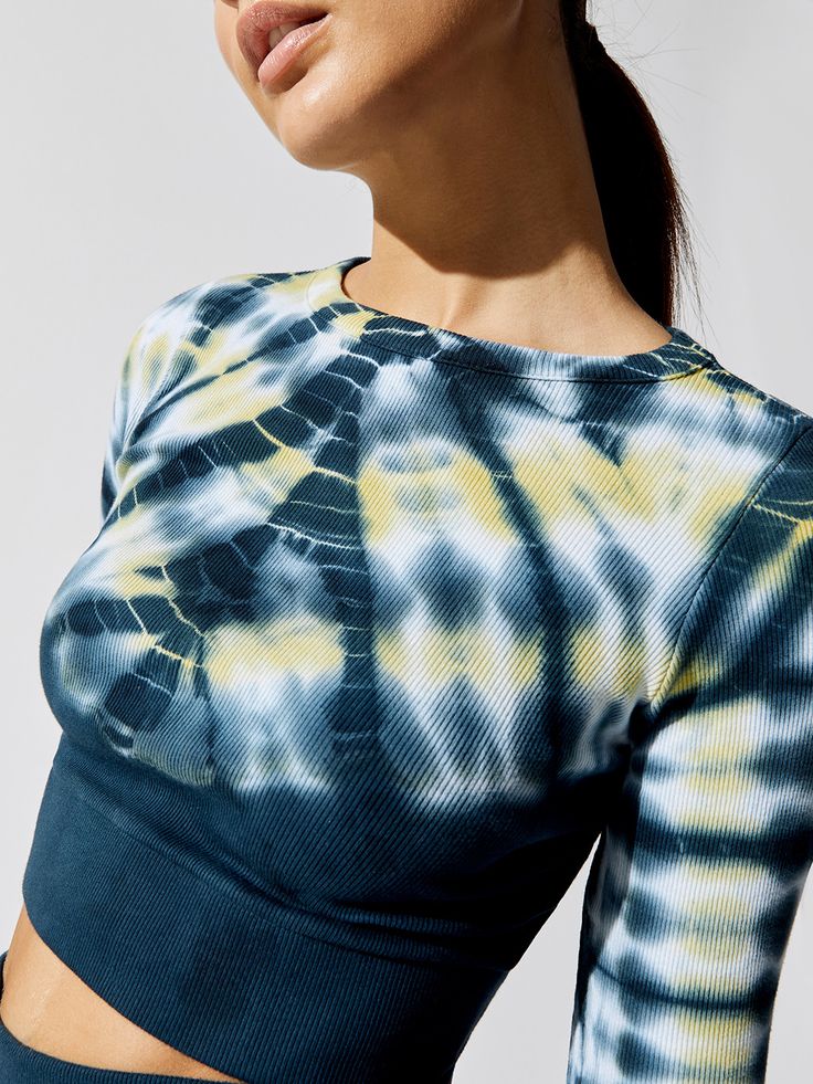 a woman wearing a tie dye top with her hands on her hips and looking off to the side