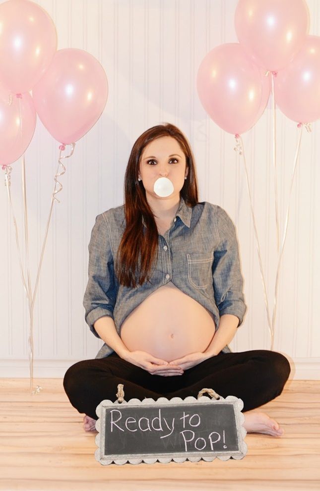 a pregnant woman is sitting on the floor with balloons and a sign reading ready to pop