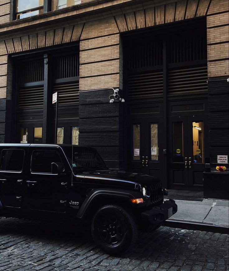 a black jeep parked in front of a tall building on a cobblestone street