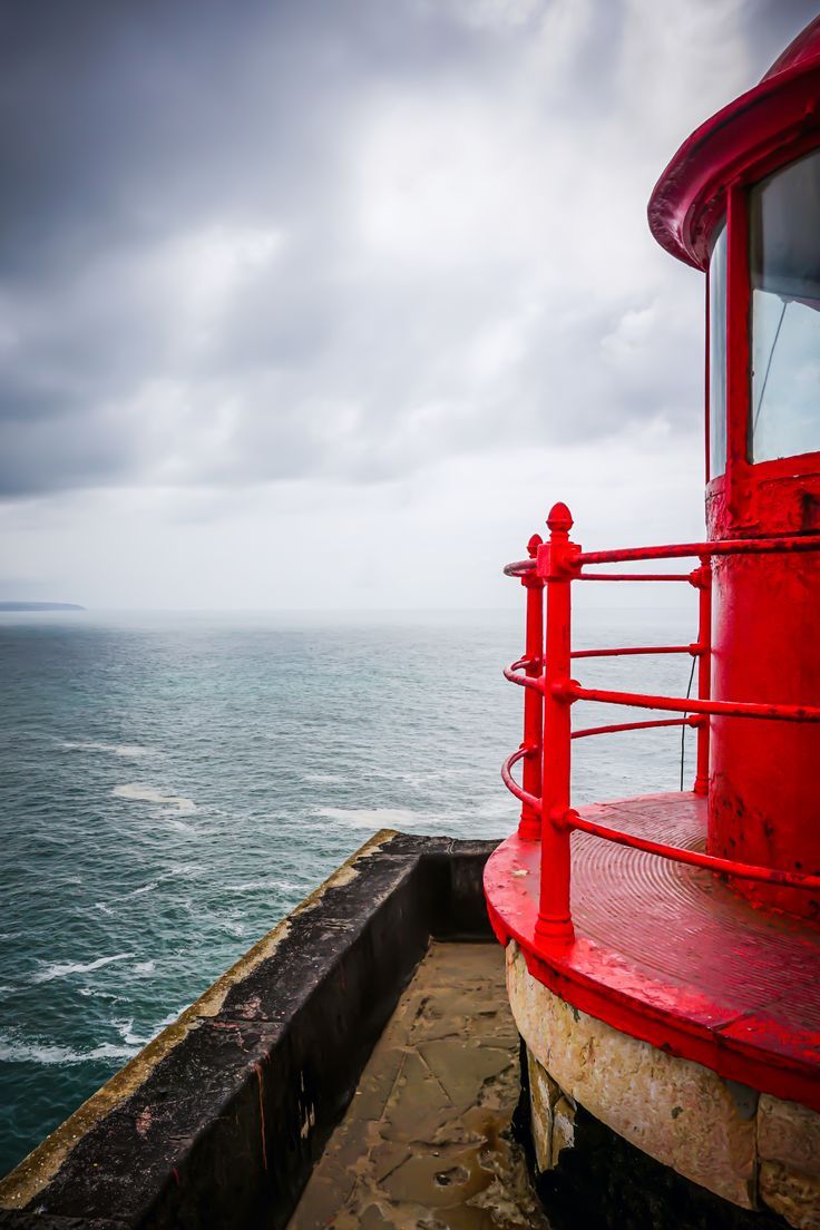 a red boat sitting on top of a pier next to the ocean under a cloudy sky