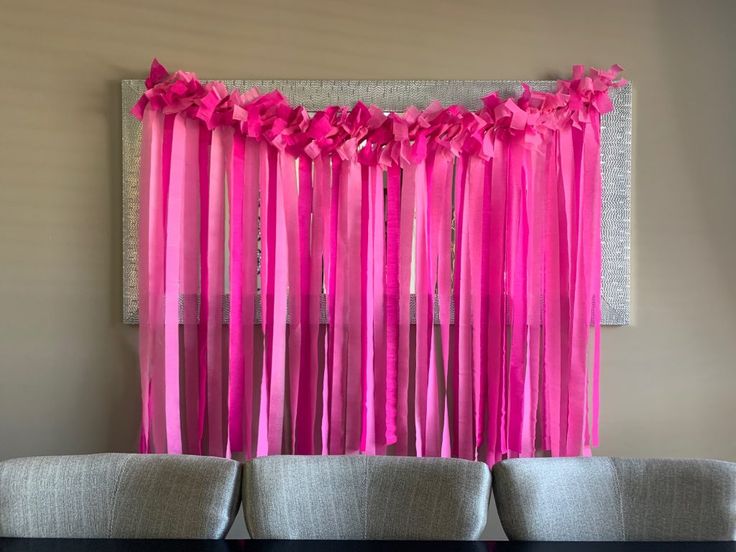 pink streamers are hanging over the back of two chairs in front of a wall