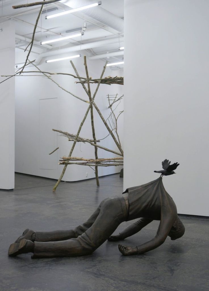 a sculpture is laying on the floor in front of a white wall with branches sticking out of it