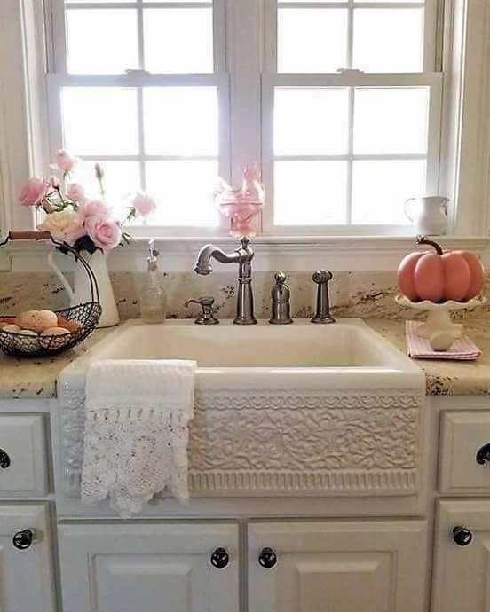 a white kitchen sink sitting under a window next to a vase filled with pink flowers