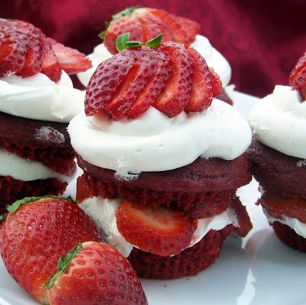 strawberries and whipped cream on top of cupcakes are arranged on a white plate