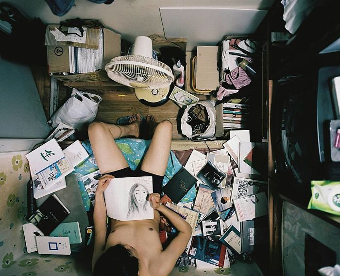 a person laying on the floor surrounded by clutter and books in a messy room