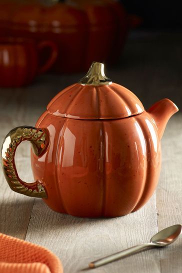 an orange teapot sitting on top of a wooden table next to silver spoons