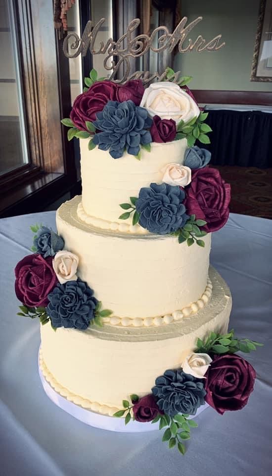 a three tiered cake with purple and blue flowers on the top is sitting on a table