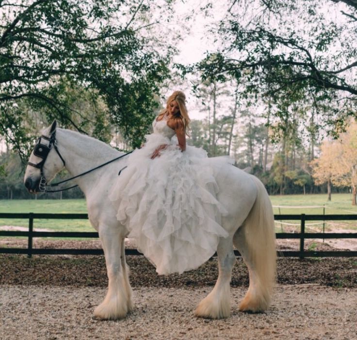 a woman in a white dress riding on the back of a horse