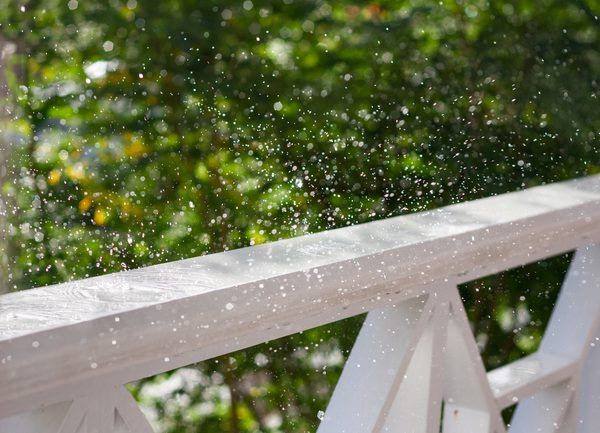 the rain is falling down on a white wooden bench with green trees in the background