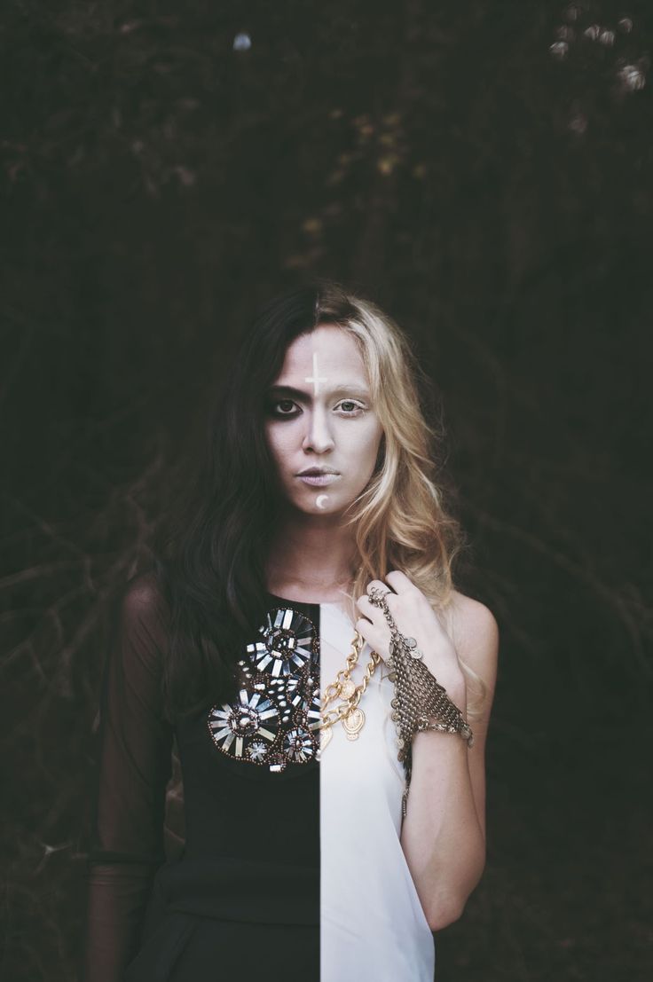 a woman standing in front of a tree with her hands on her chest and face painted white