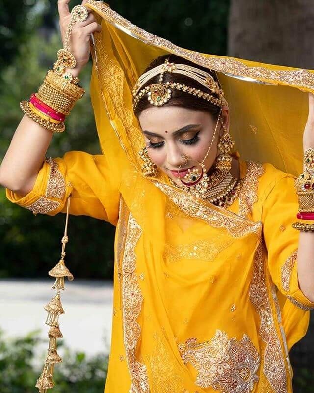 a woman in a yellow outfit with jewelry on her head and hands behind her head