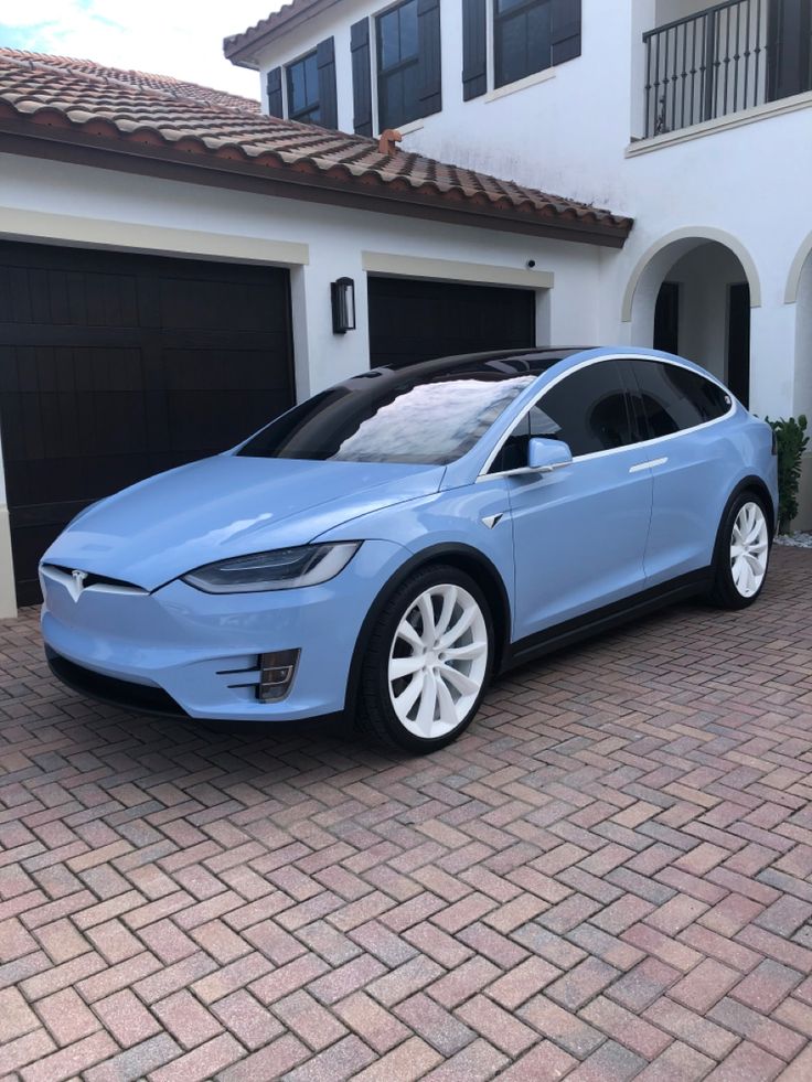 a blue electric car parked in front of a white house with two garage doors open