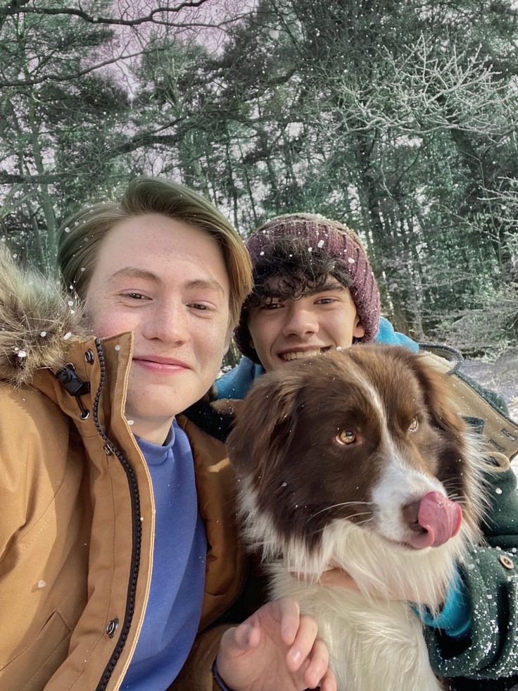 two people and a dog posing for a photo in the snow with trees behind them