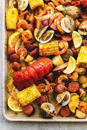 lobster, corn on the cob, and potatoes in a baking pan with lemon wedges