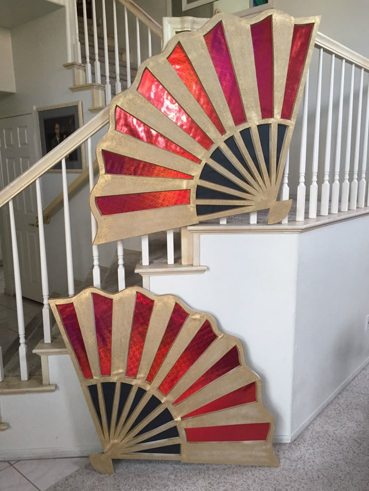 two red and gold fans sitting on top of a white stair case next to a banister