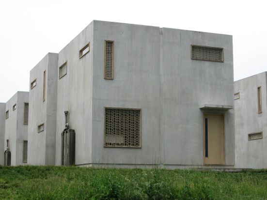 a row of concrete buildings sitting on top of a lush green field next to tall grass