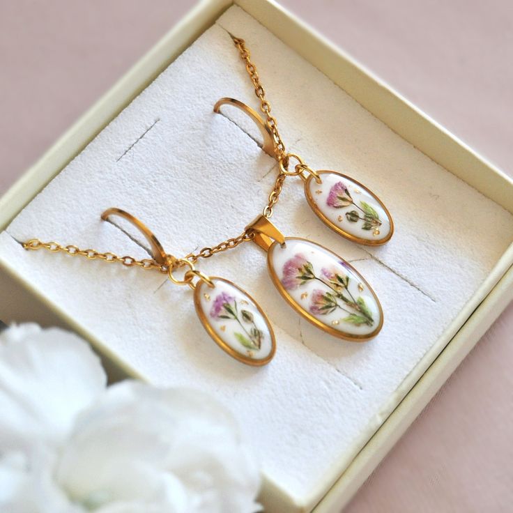 three pieces of jewelry in a box with white flowers on the bottom and gold chain