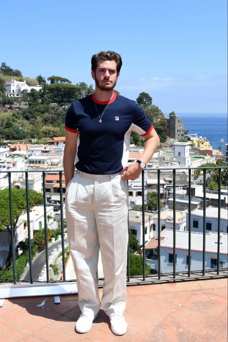 a man standing on top of a balcony next to a railing with his hands in his pockets