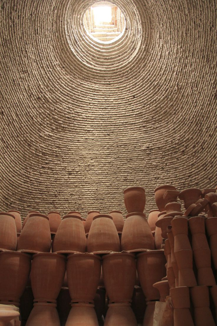 many clay pots are stacked together in a room with a round window above them and the ceiling is made of woven wicker