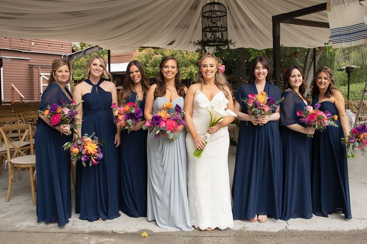 a group of women standing next to each other in front of a tent with flowers