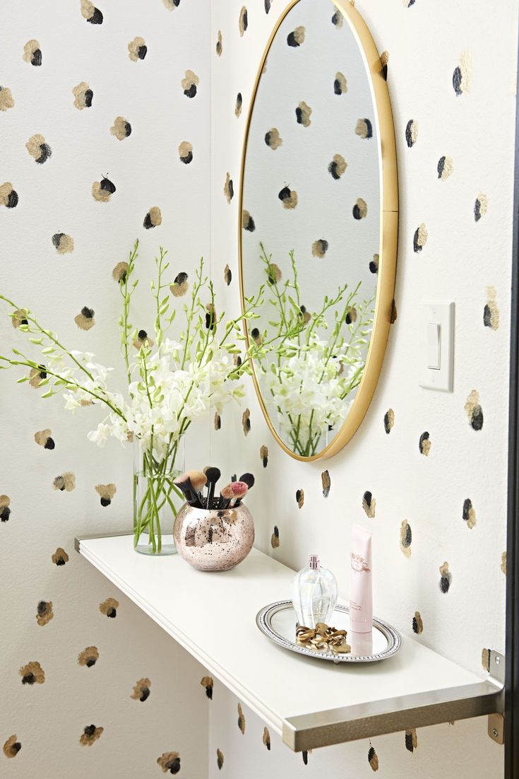 a white table topped with a mirror and vase filled with flowers next to a wall