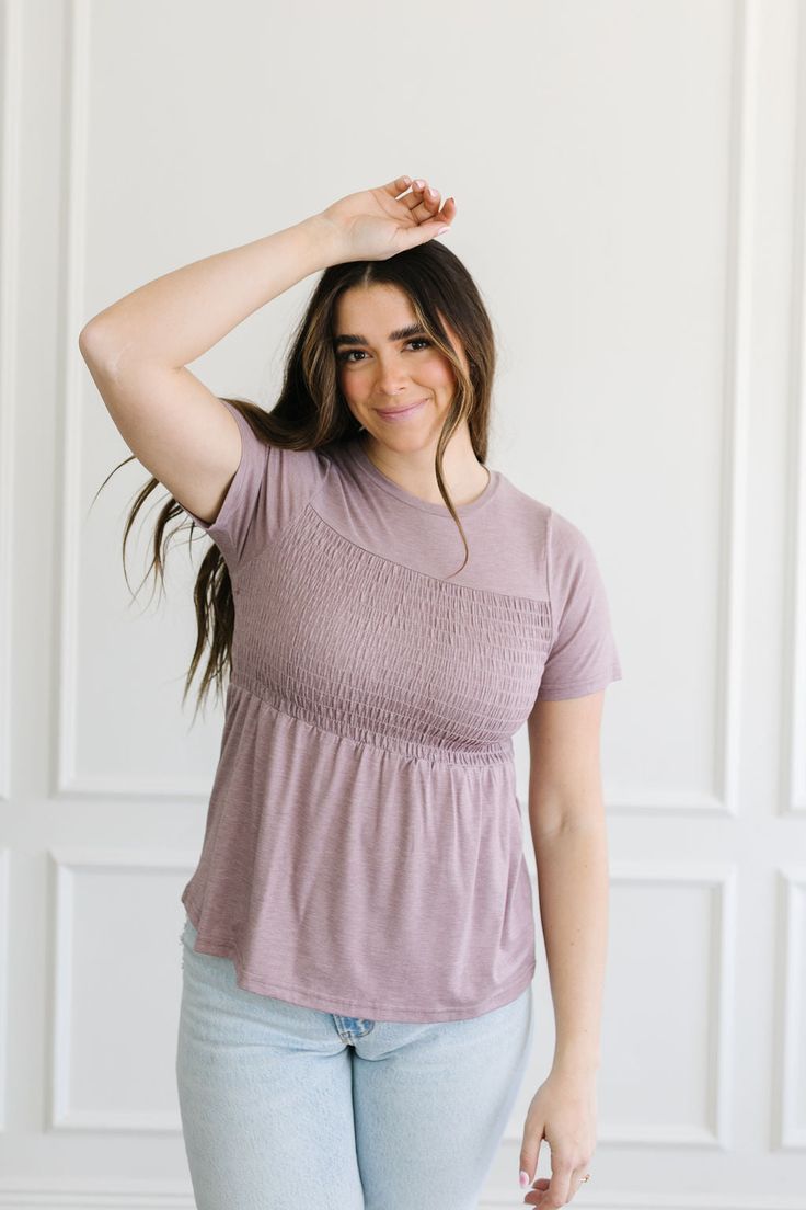 Introducing the Dana Top: its sweet lavender hue and soft fabric make it a dream to wear! Look no further for a top that's both stylish and comfortable, with smocked detail in the bust area and short sleeves for a touch of detail. Look luxurious and feel comfortable in the Dana Top! Model is wearing a size small and is 5'7". Plus model is wearing a size 1X and is 5'8". Size Chart Length Bust S 23" 30" M 23.5" 32" L 24" 34" 1x 26.5" 41" 2x 27" 46" 3x 27" 49" *All measurements are approximate and Casual Tops With Elastic Waistband And Fitted Design, Summer Stretch Tops With Gathered Waist, Casual Tops With Gathered Waist And Short Sleeves, Stretch Purple Feminine Tops, Feminine Fitted Lavender Top, Purple Stretch Feminine Top, Summer Tops With Gathered Waist And Short Sleeves, Short Sleeve Tops With Gathered Waist For Summer, Fitted Casual Top With Gathered Waist