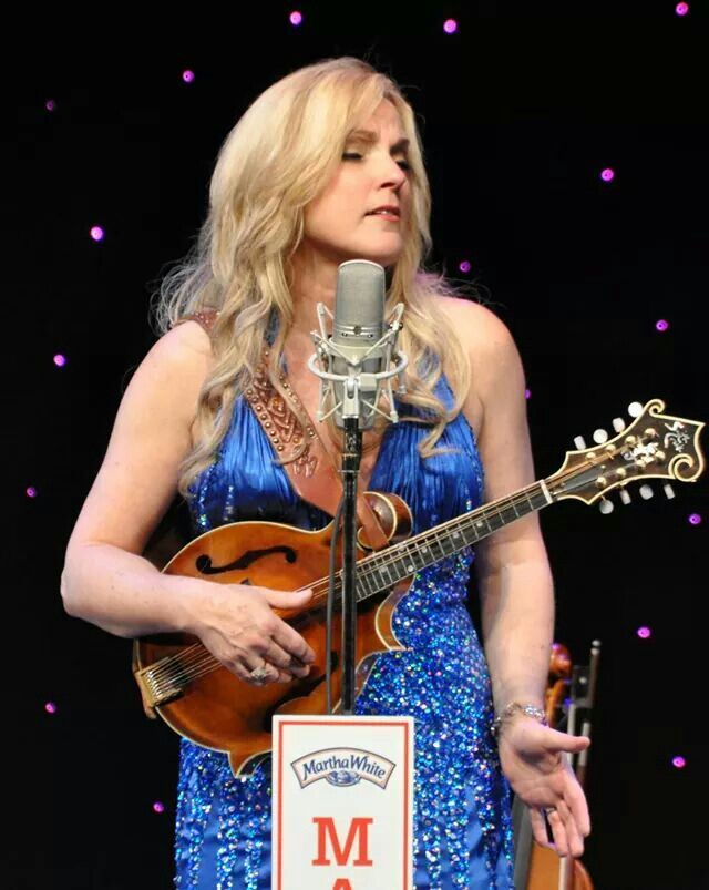 a woman in a blue dress holding a guitar and singing into a microphone on stage