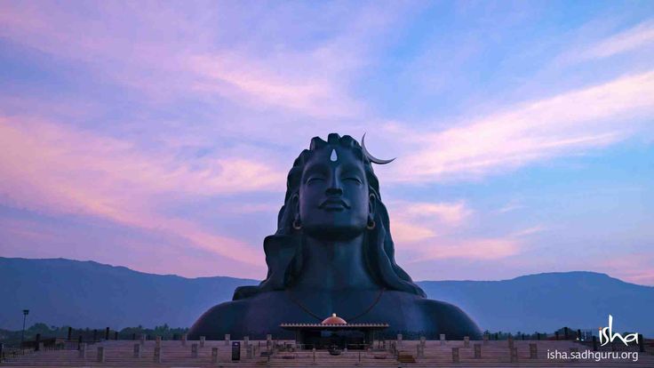 there is a large statue in front of the sky with mountains in the back ground