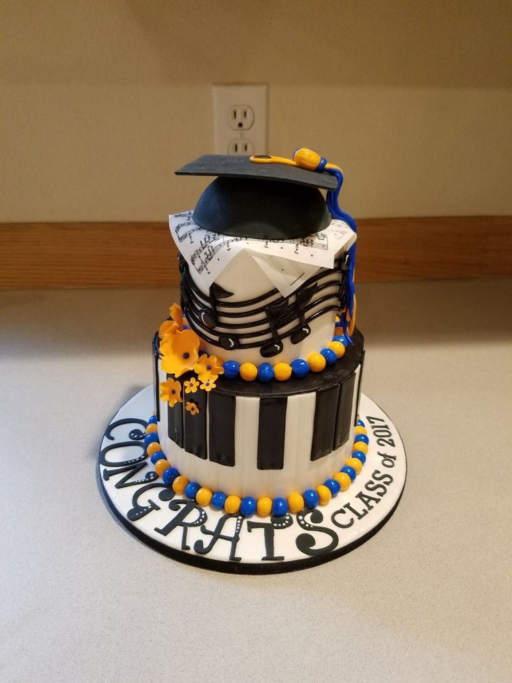 a graduation cake decorated with black and white stripes, blue and yellow decorations, and a cap on top