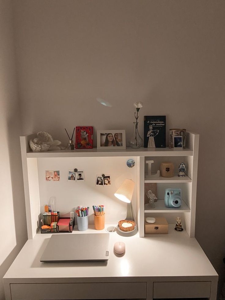 a white desk topped with a laptop computer next to a lamp and bookshelf