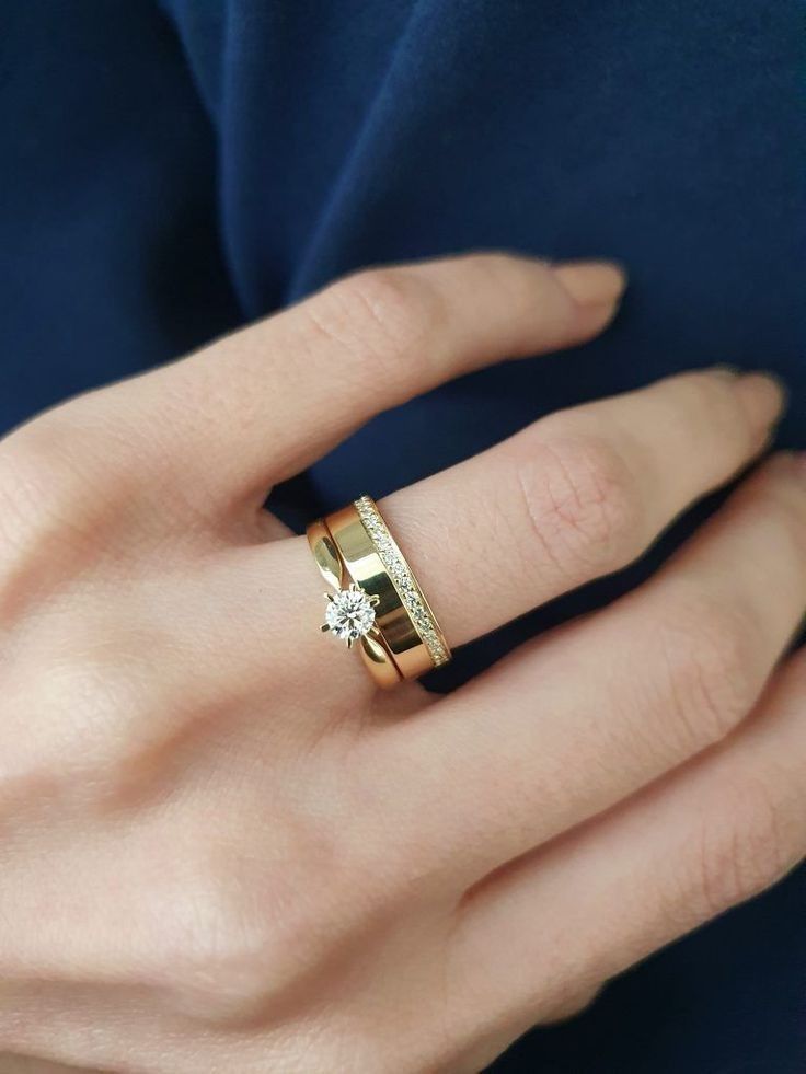 a woman's hand wearing a gold ring with a diamond in the middle and two rows of diamonds on each band