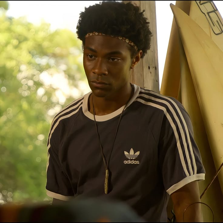 a man with dreadlocks standing next to a surfboard