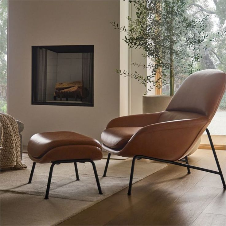 an eames chair and ottoman in front of a fireplace with a view of the woods