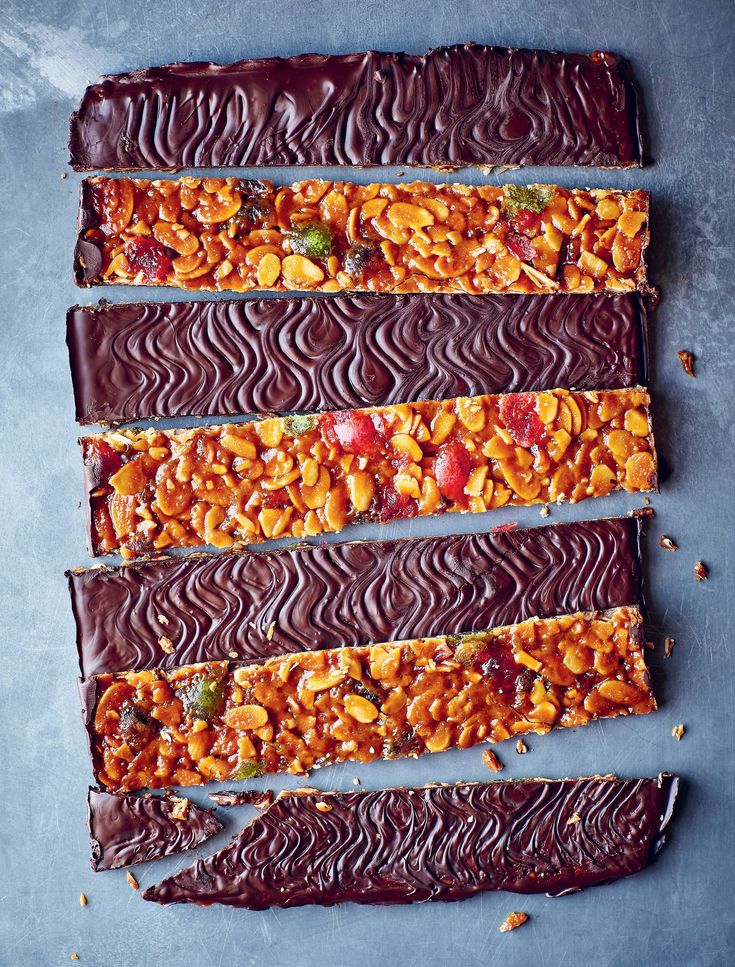 chocolate bars with nuts and dried fruit on top, lined up in horizontal rows against a gray background