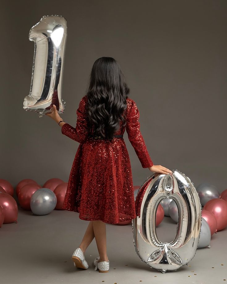 a girl in a red dress is holding a balloon and the number six stands next to balloons