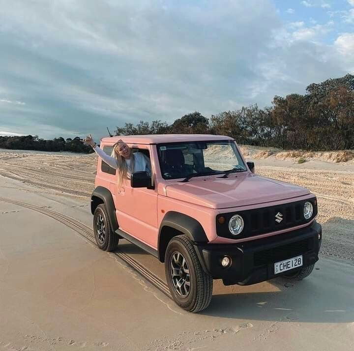 a pink truck parked on the beach with a man in it's seat looking out the window