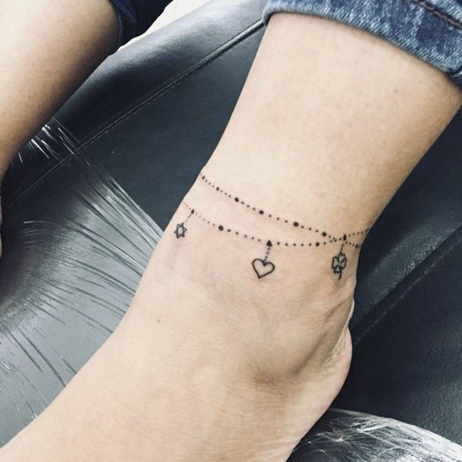 a woman's foot with a chain and hearts tattoo on it