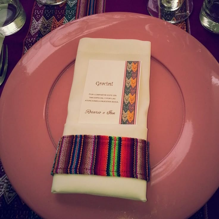 a pink plate topped with a striped napkin and place setting on top of a purple table cloth