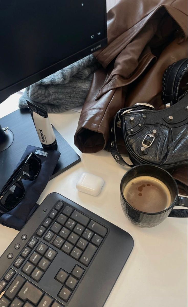 a computer keyboard sitting on top of a desk next to a cup of coffee and purse