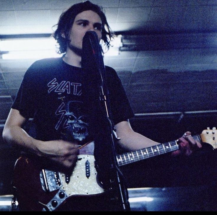 a man with long hair playing guitar in front of a microphone and singing into a mic