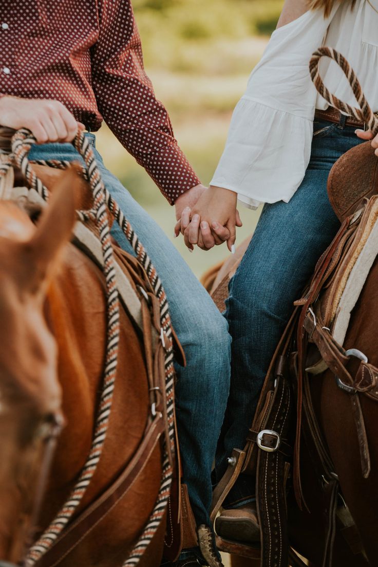 a man and woman riding on the back of brown horses in an open field, holding hands