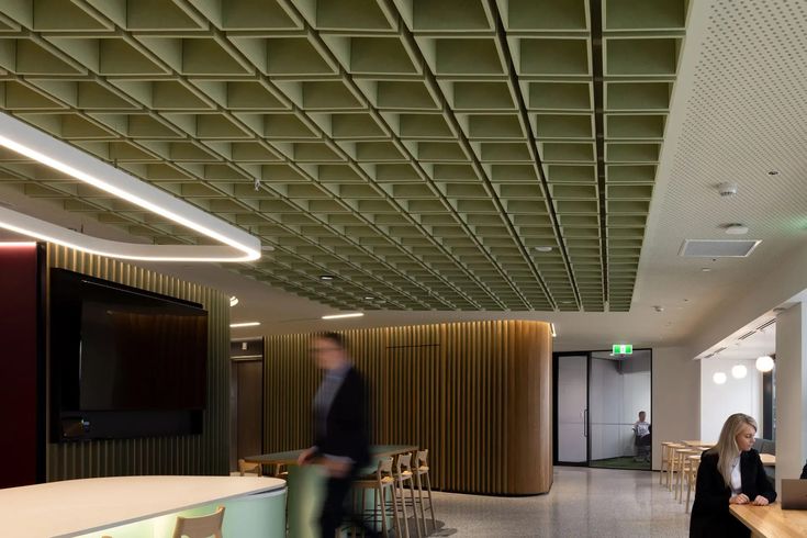 people are sitting at tables in an office building with wood paneling on the ceiling