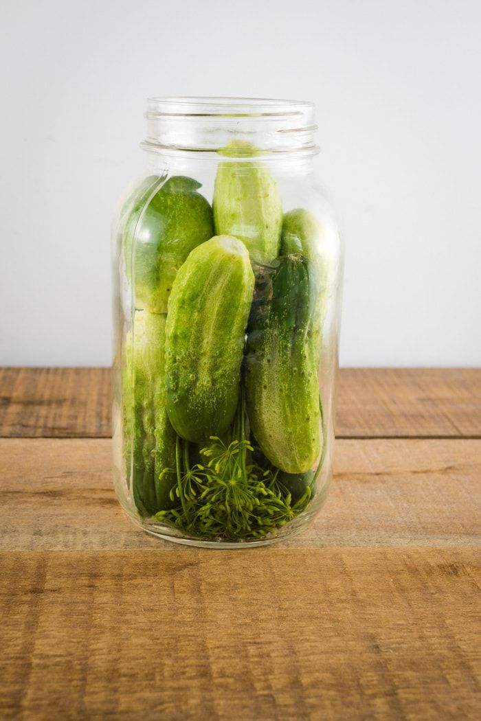 pickles in a glass jar on a wooden table with water and grass inside them