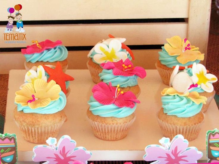 cupcakes with blue frosting and colorful flowers on them sitting on a table